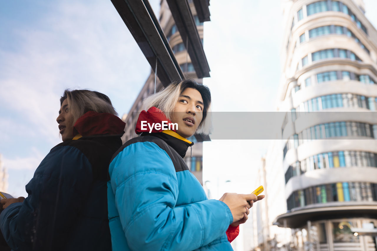 Young man with smart phone looking away in city