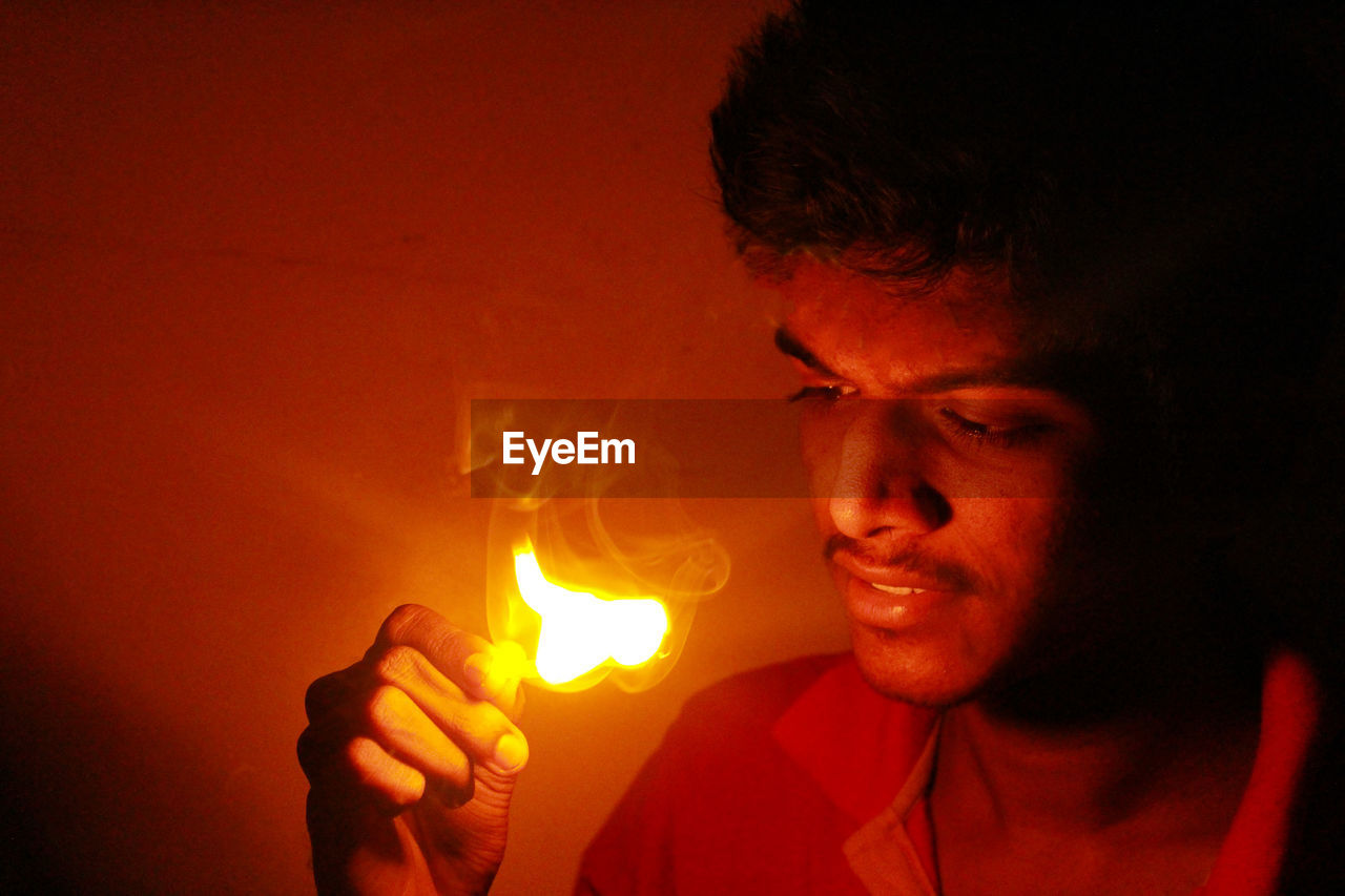 Close-up of young man holding lit matchstick