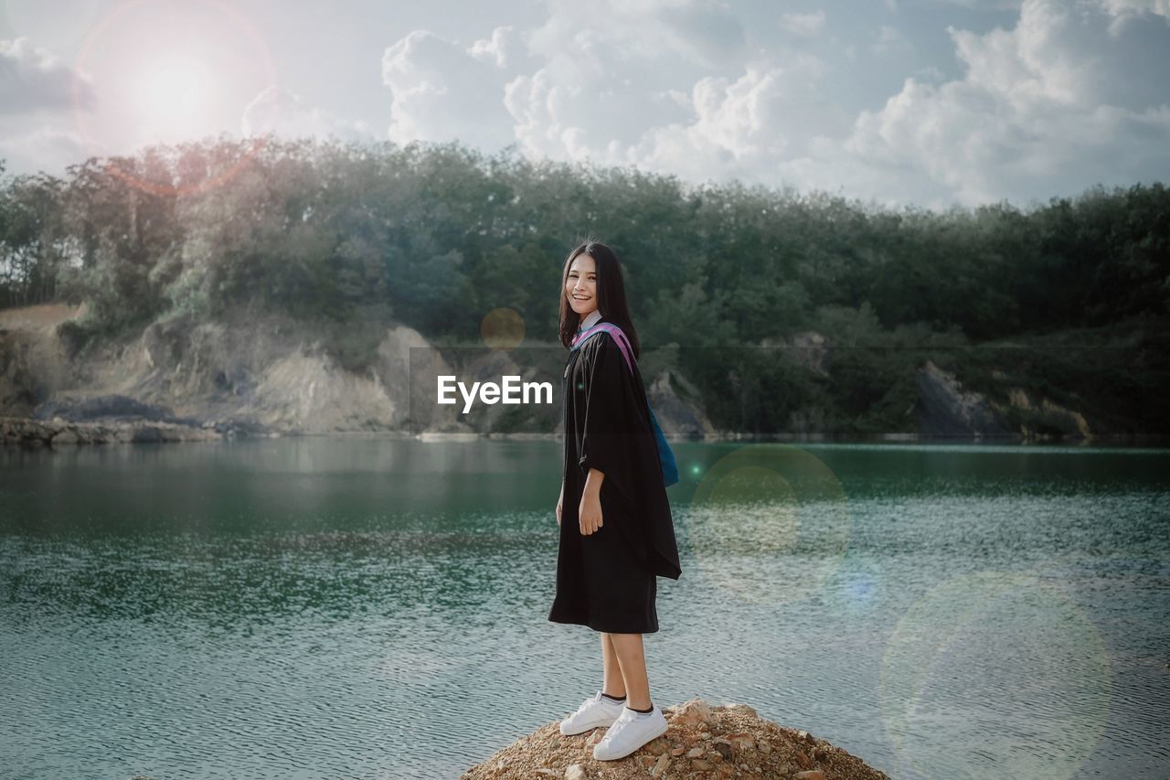 Smiling young woman standing by lake against mountain