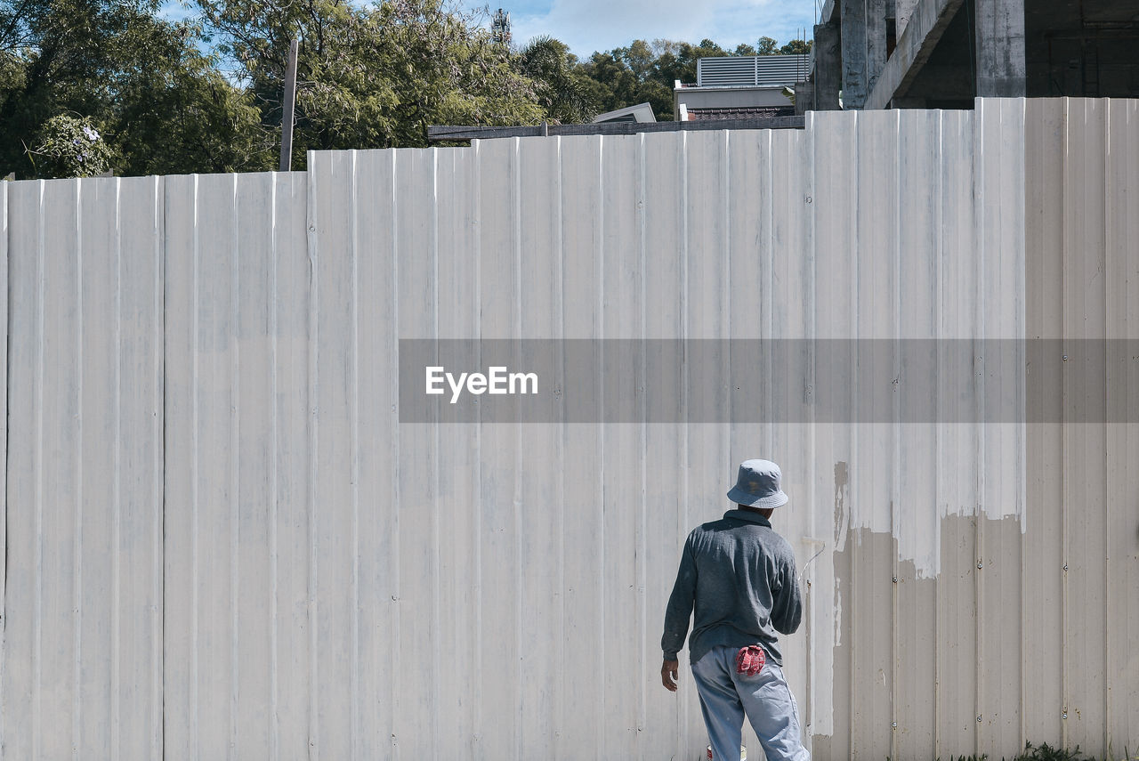 Rear view of man painting wall outdoors