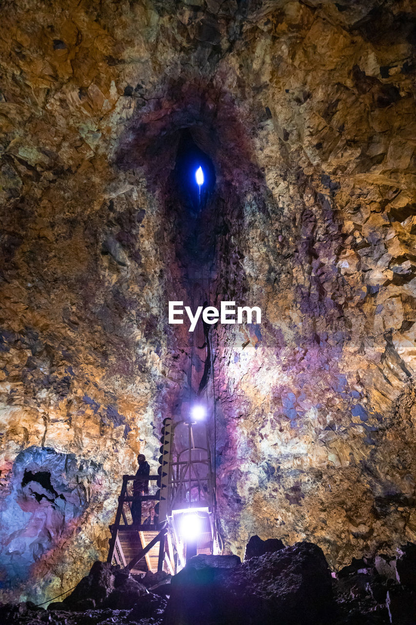 LOW ANGLE VIEW OF ILLUMINATED MAN STANDING IN CAVE