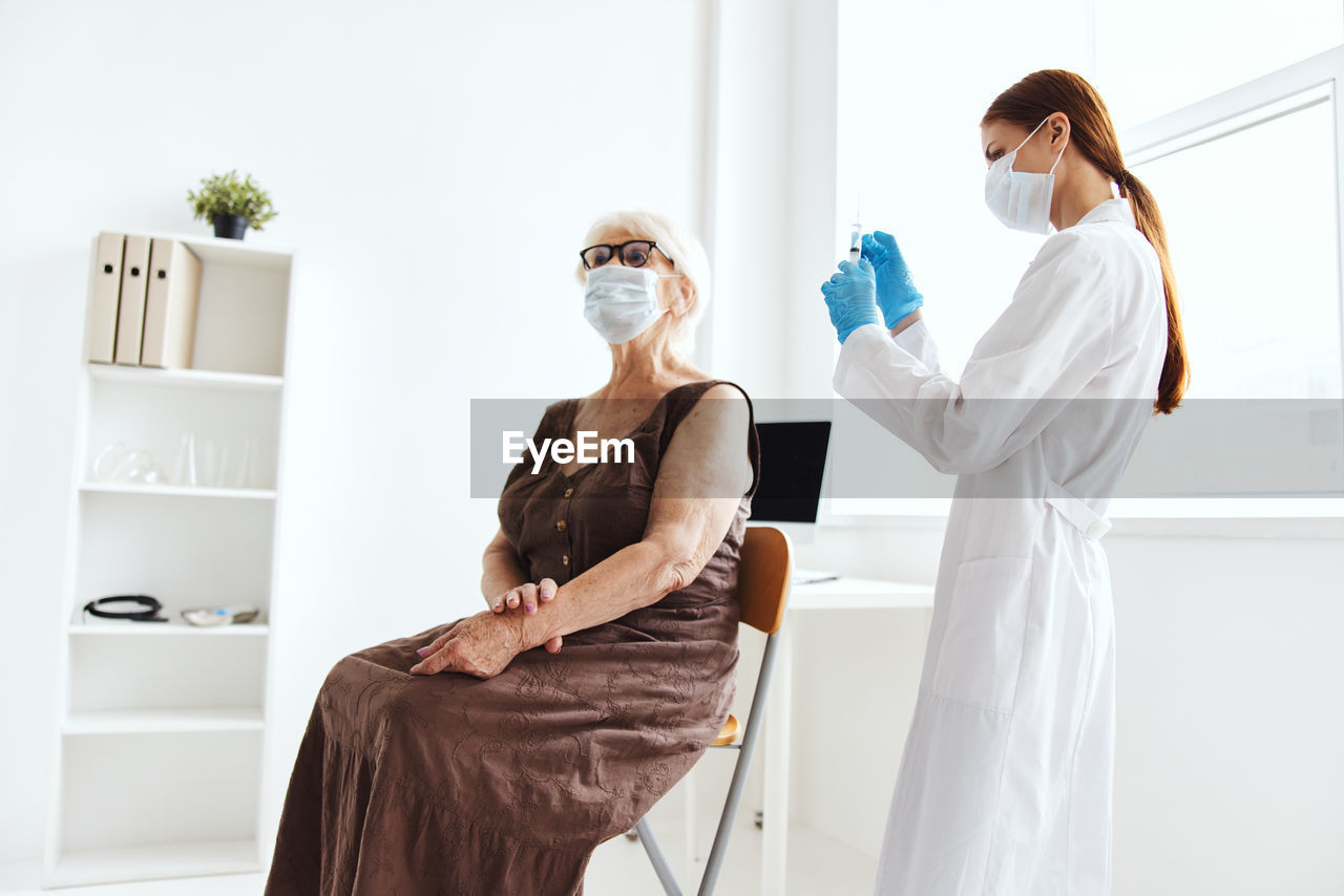 Doctor wearing mask vaccinating patient at hospital