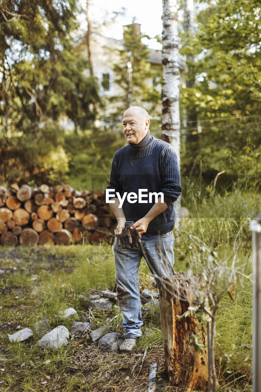 Smiling gay man holding gardening gloves while walking on field