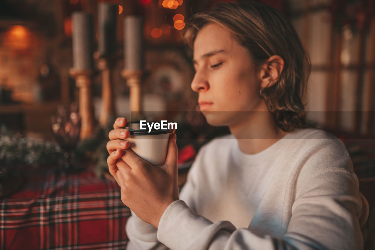 Portrait of candid authentic smiling handsome boy teenager using mobile phone at xmas home interior