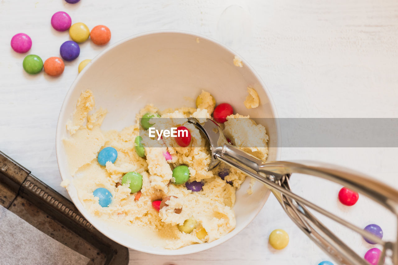 Directly above shot of raw cookies with candies in bowl on table