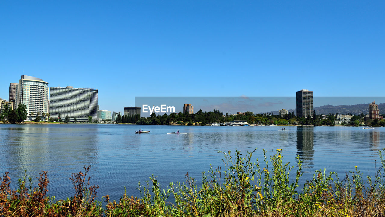 Buildings by lake against blue sky