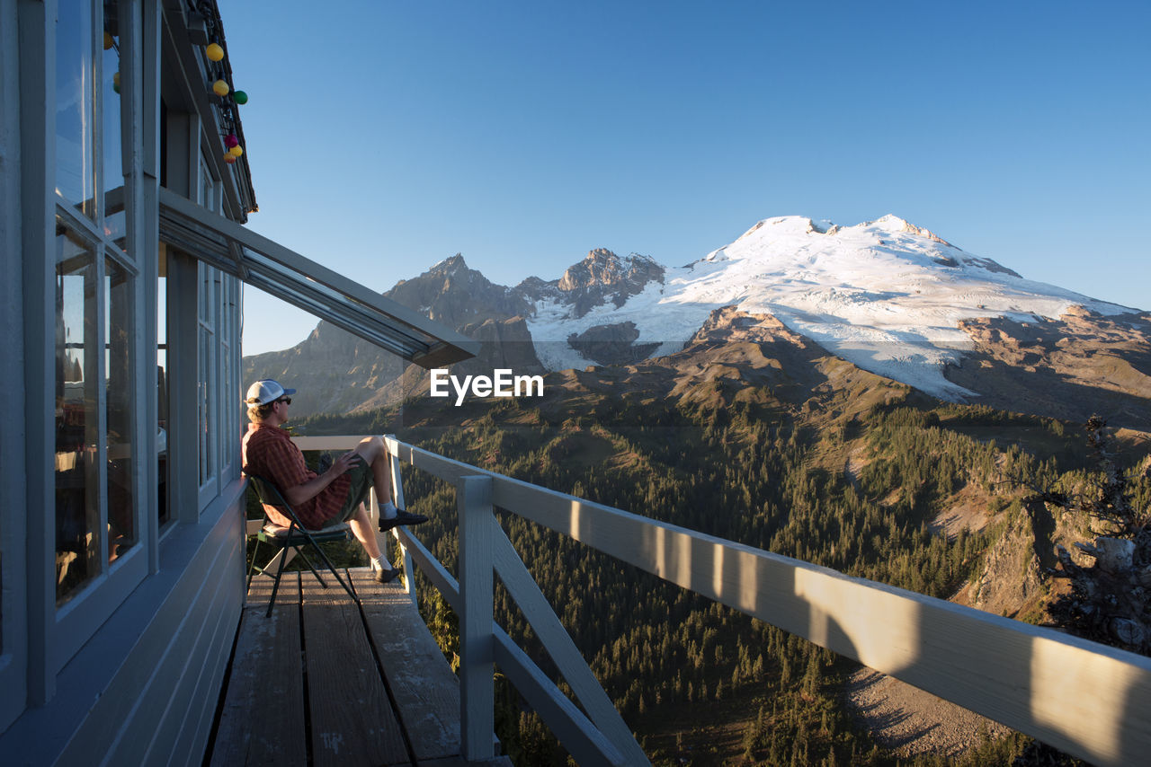 Side view of man sitting on balcony of cottage against mountains