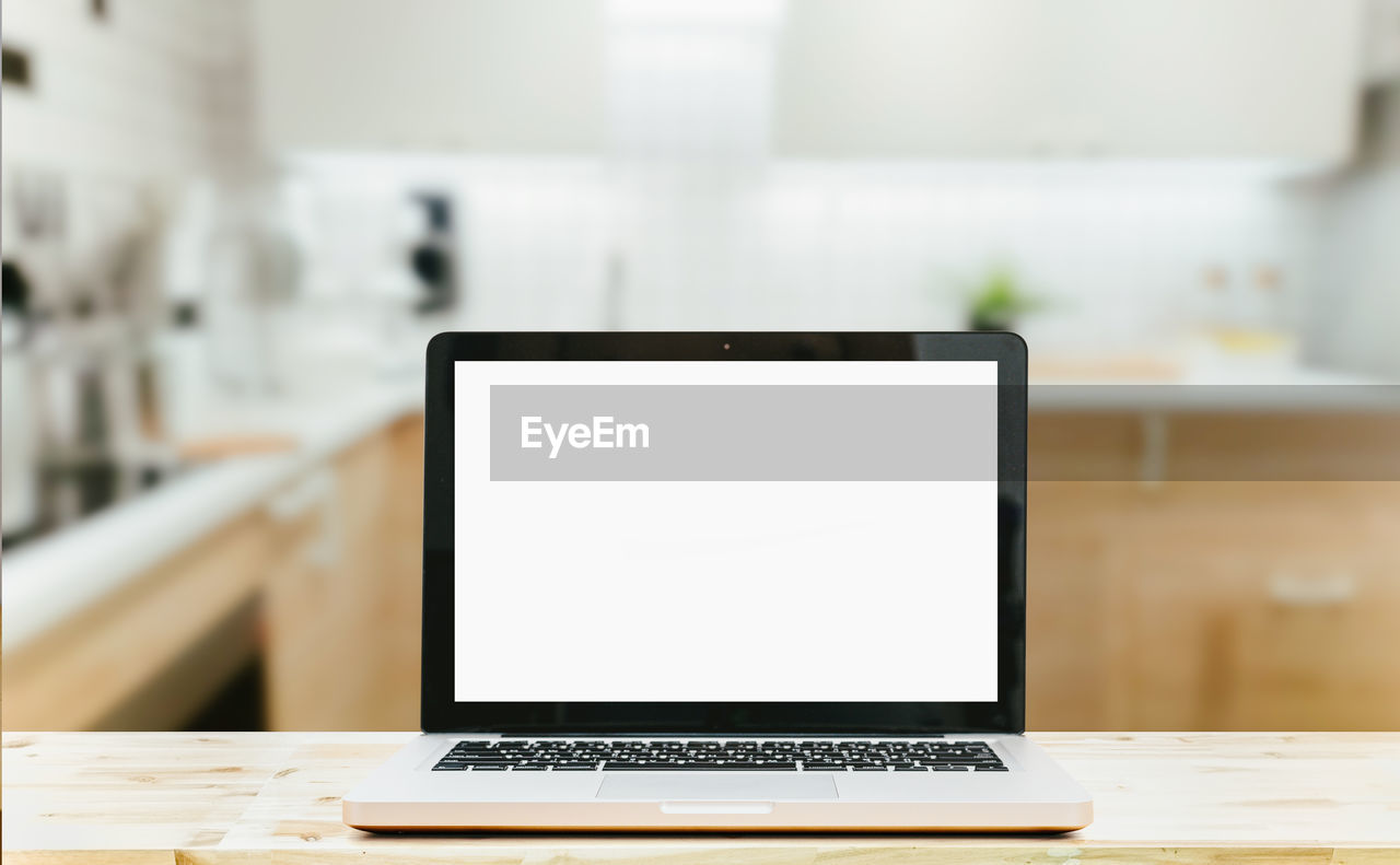 Modern computer,laptop with blank screen on wood table top on blurred kitchen background