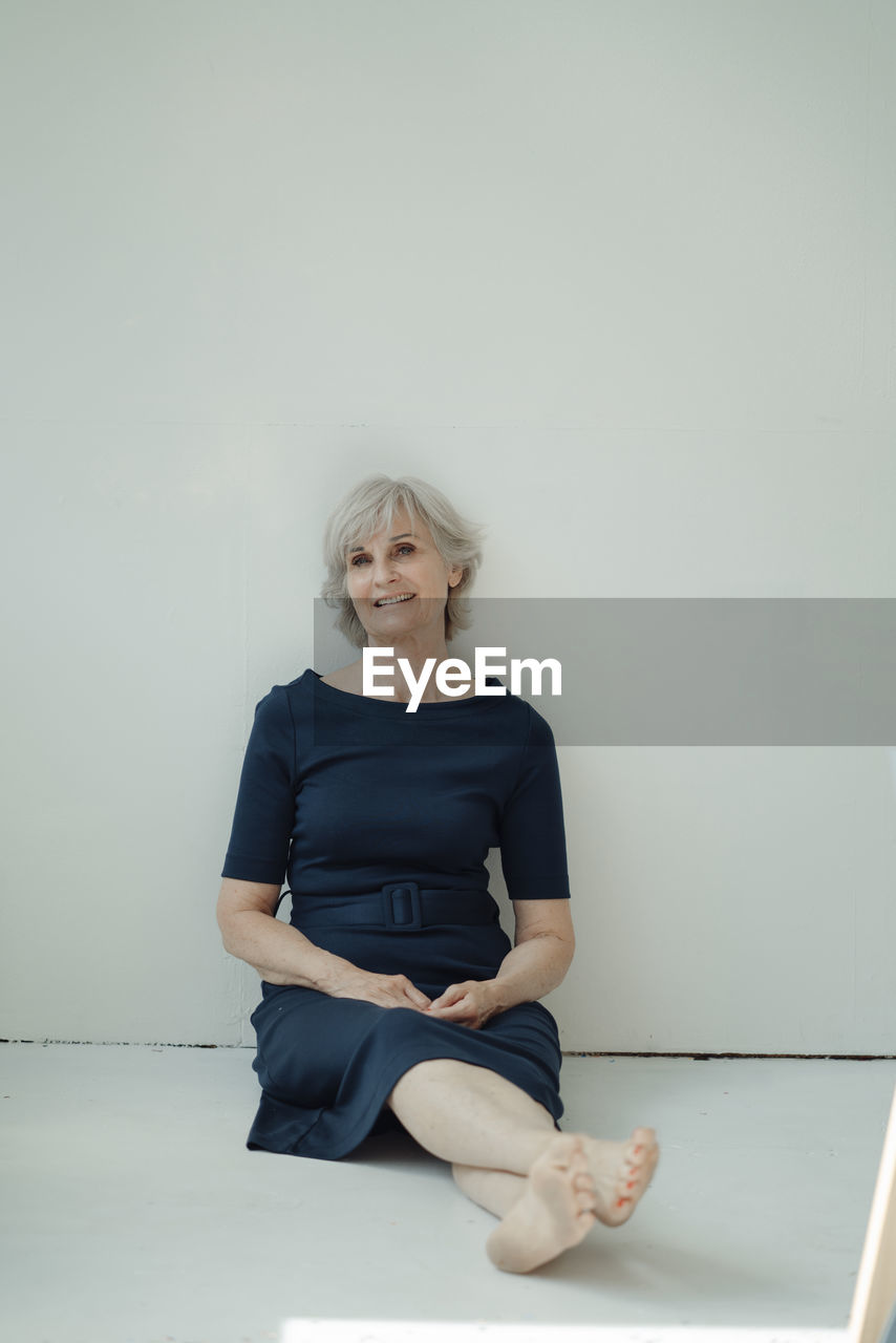 Happy senior businesswoman sitting in front of wall