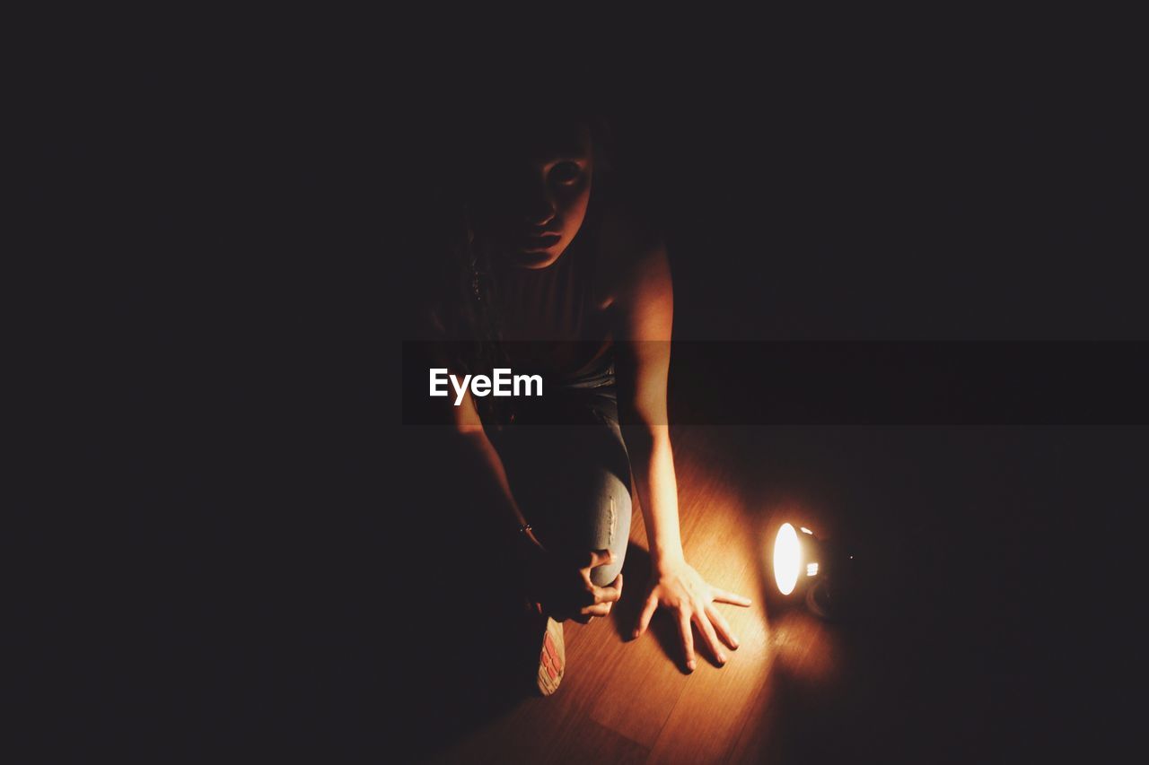 High angle portrait of young woman sitting by illuminated flashlight on floorboard