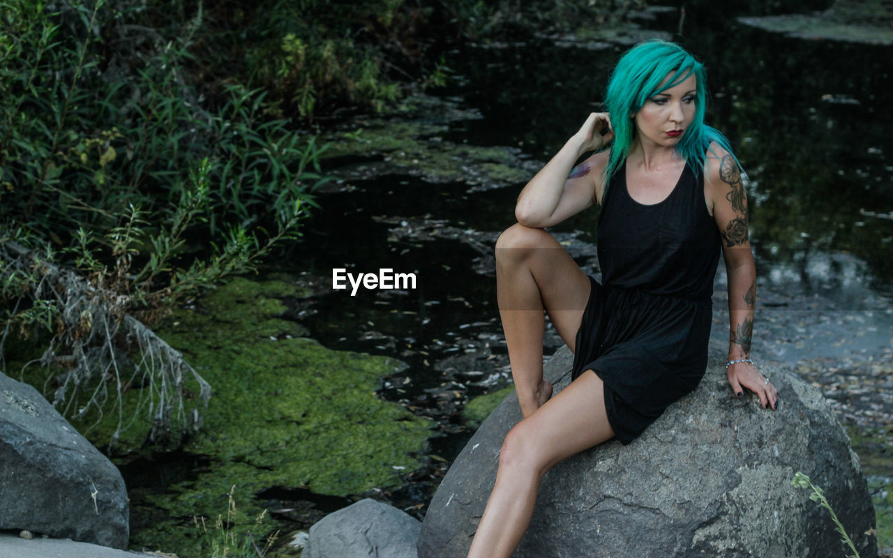 Punk woman sitting on rock against pond