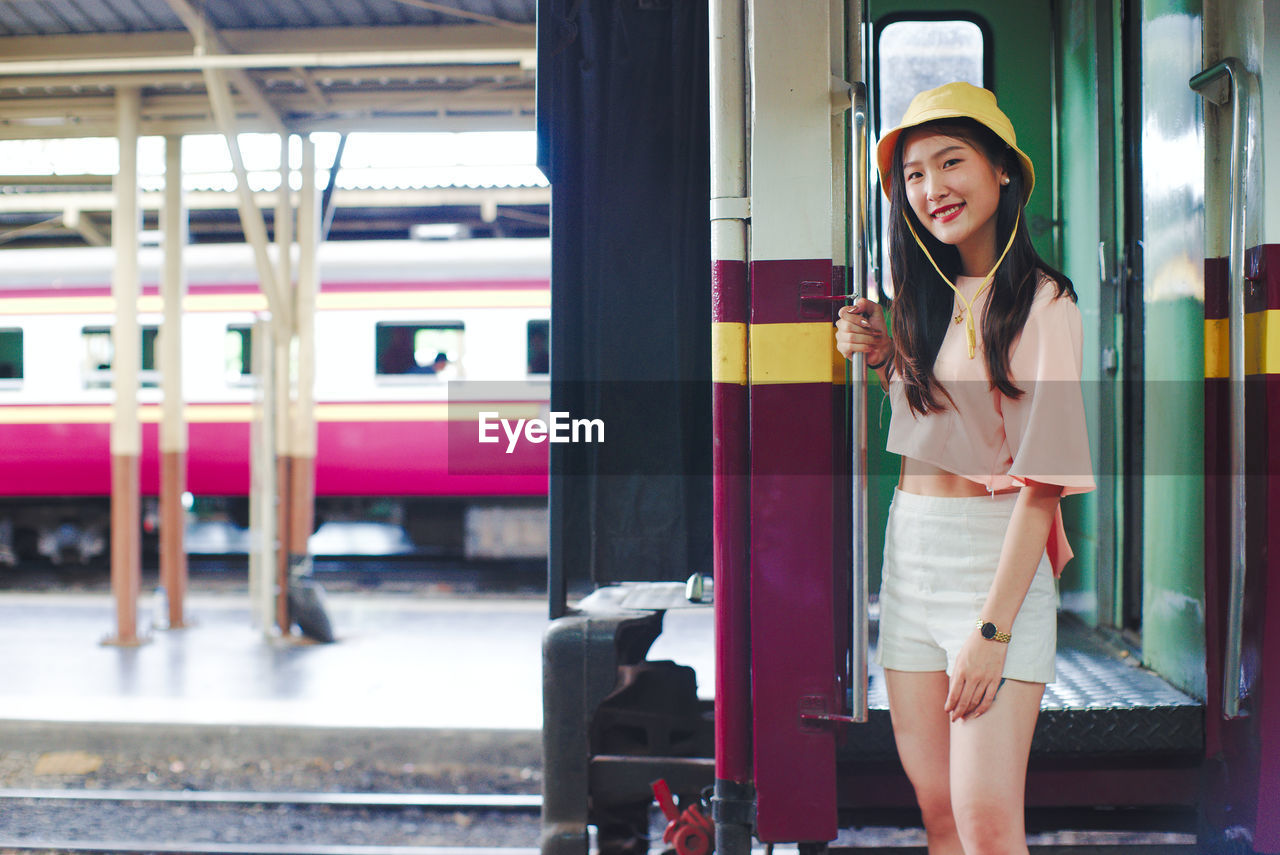 Portrait of smiling young woman standing at railroad station