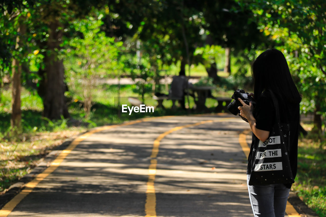 Woman looking at camera while standing on road amidst trees
