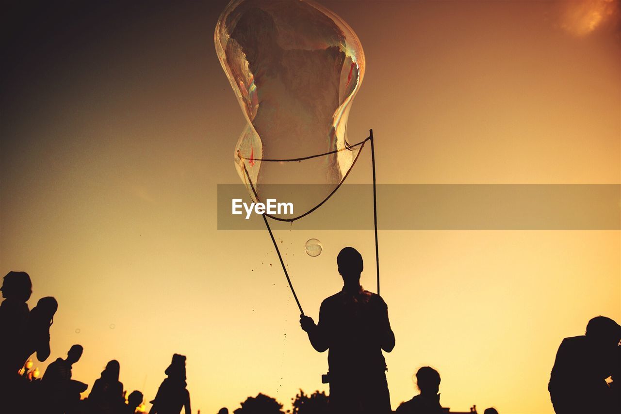 Low angle view of silhouette man blowing giant bubble from wand during sunset