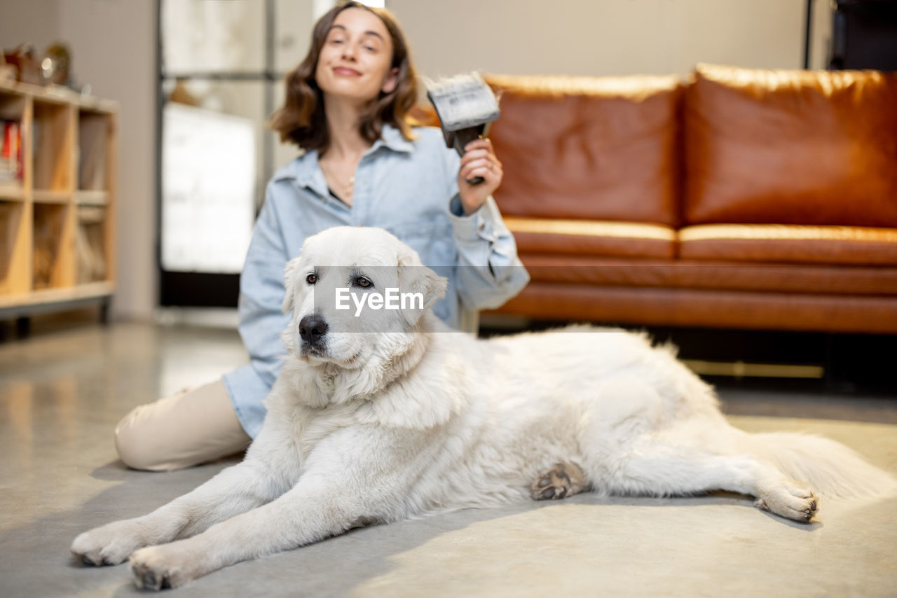 Portrait of young woman with dog sitting on sofa at home