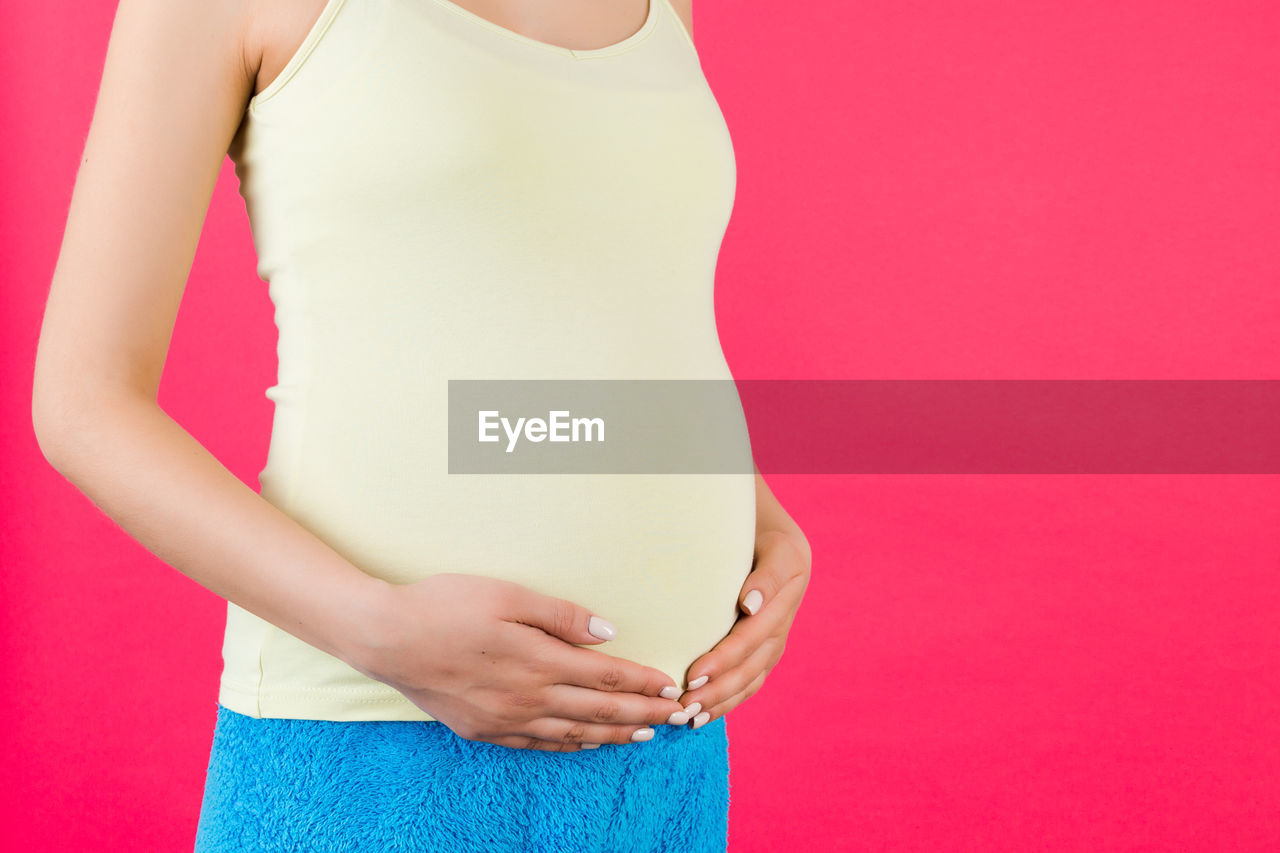 MIDSECTION OF WOMAN STANDING AGAINST PINK BACKGROUND