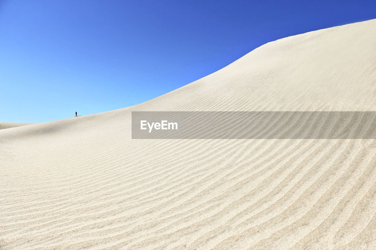 A minimalism of a tiny person at white sandy dunes and clear blue sky