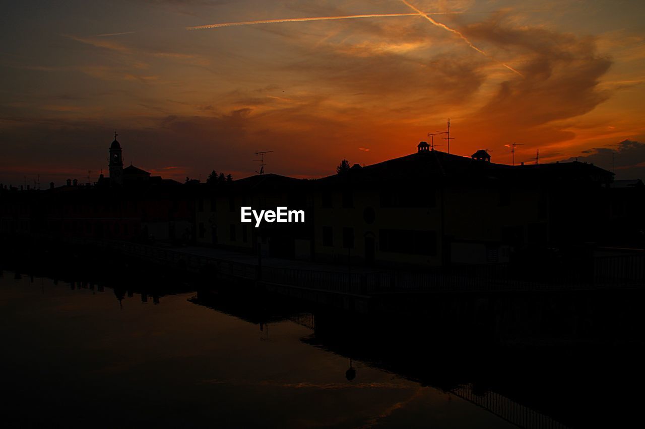 SILHOUETTE BUILDINGS BY RIVER AGAINST ROMANTIC SKY