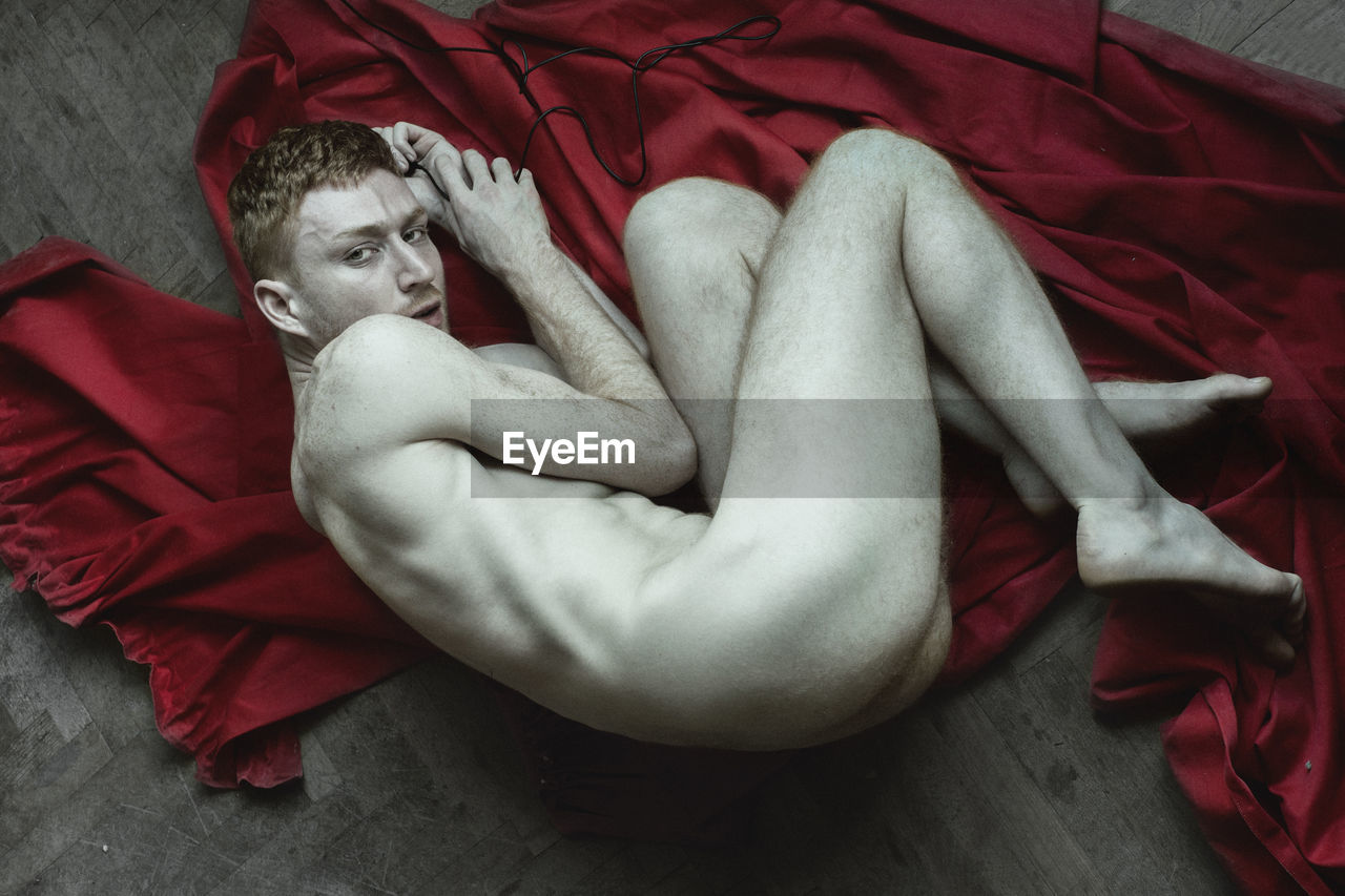 High angle portrait of naked man lying on red fabric