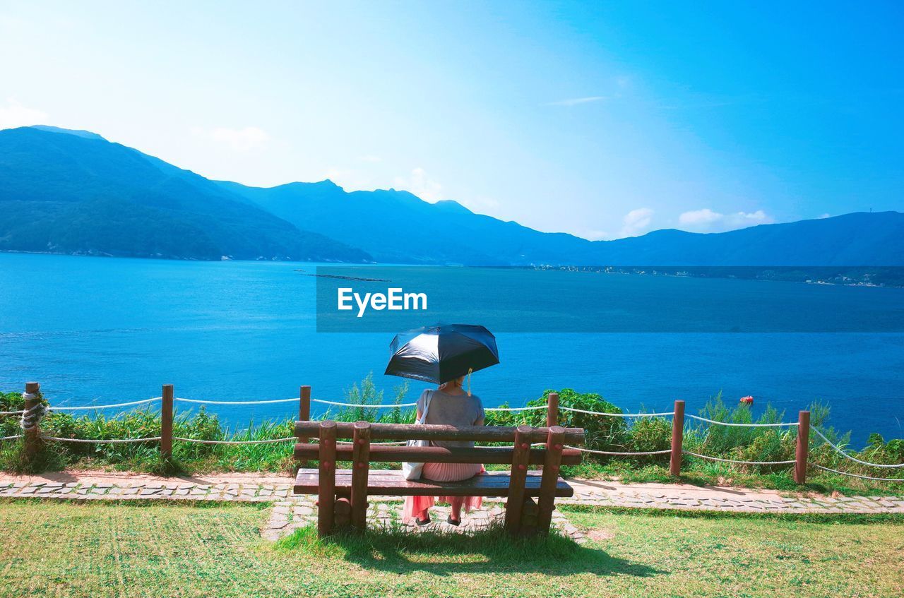 Rear view of woman sitting on bench by sea against sky