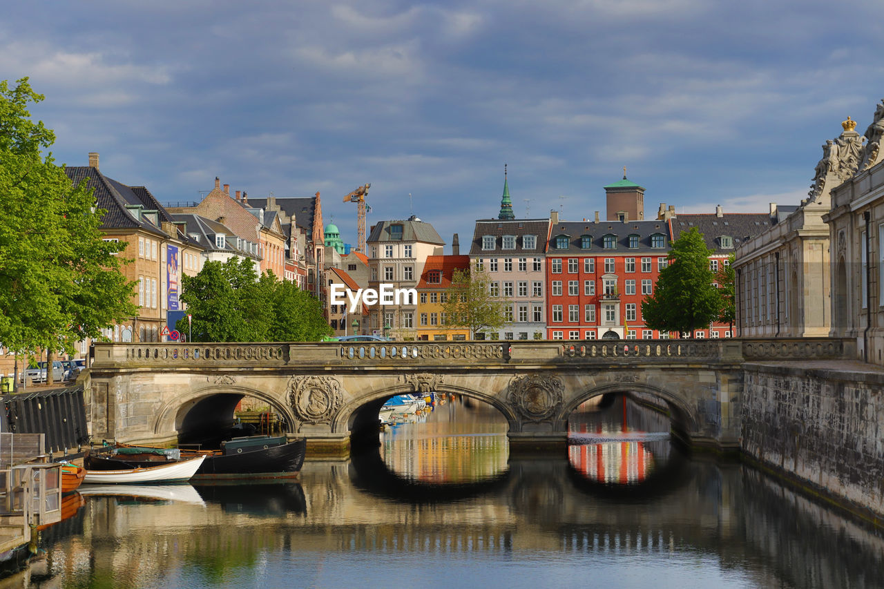 Bridge over river by buildings in city against sky