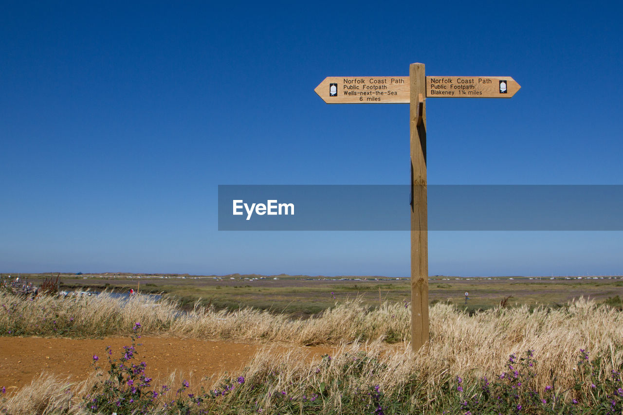 ROAD SIGN BY FIELD AGAINST CLEAR SKY