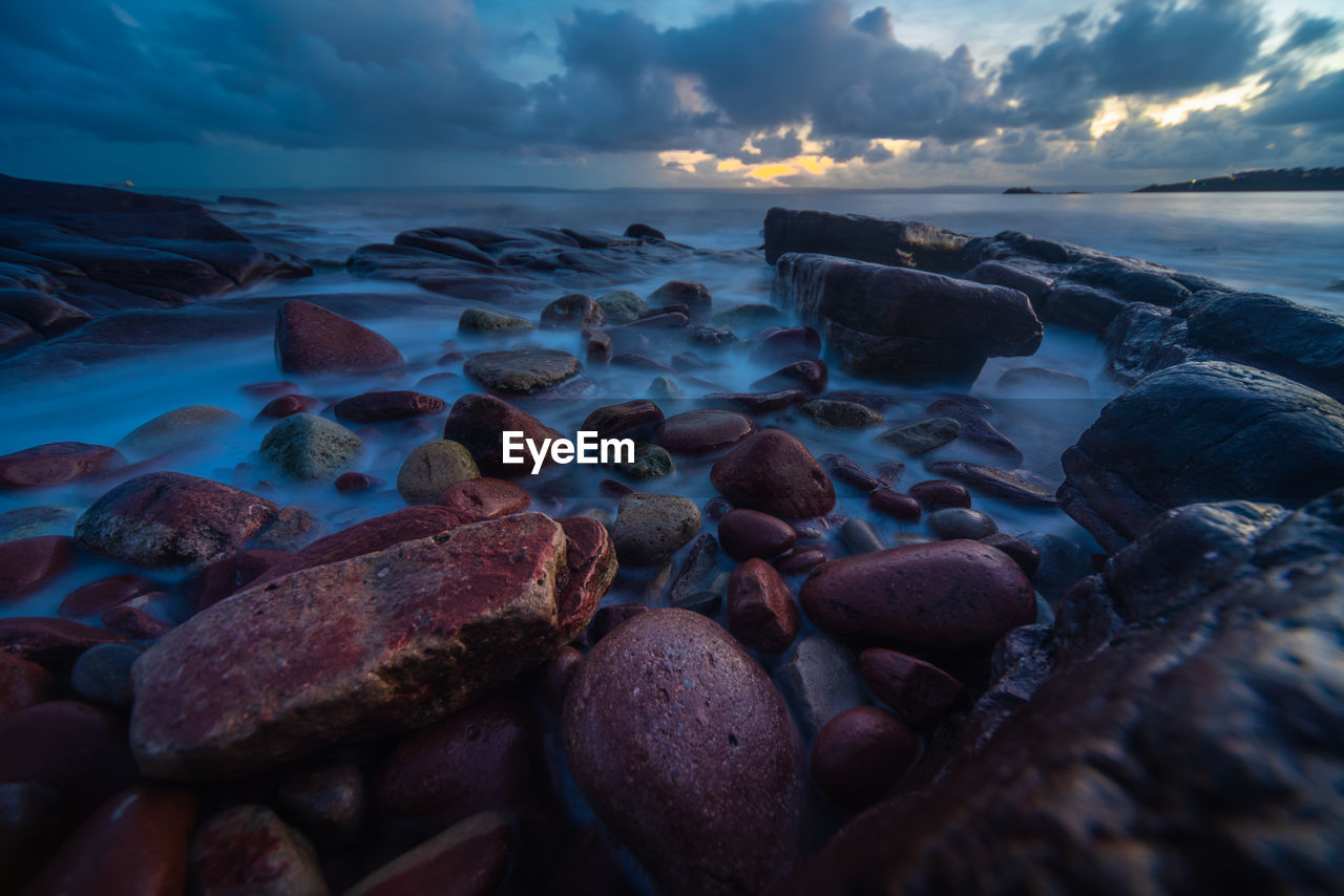 ROCKS ON BEACH AGAINST SKY AT SUNSET