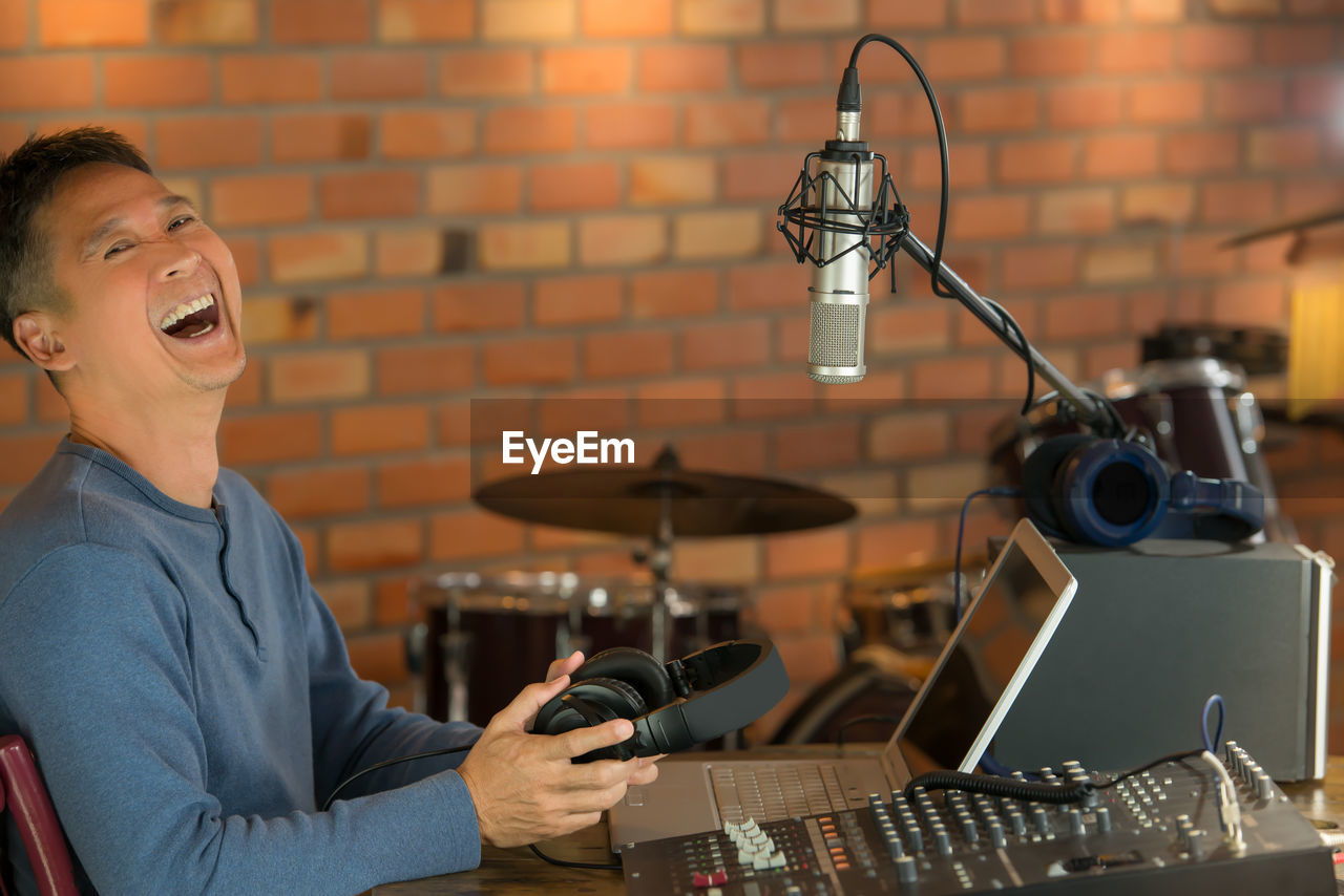 Portrait of happy man sitting by audio equipment at recording studio