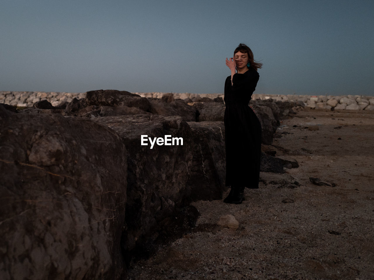 Side view of woman standing on rock against sky