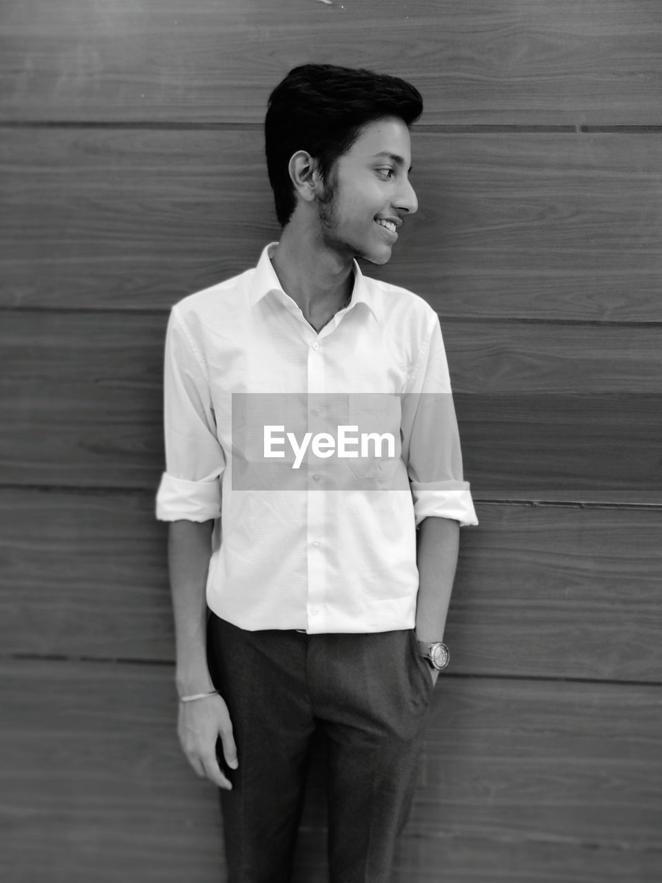 Smiling man in formalwear standing against wooden wall