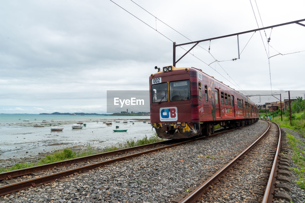 transportation, rail transportation, railroad track, track, mode of transportation, sky, cloud, train, public transportation, nature, vehicle, travel, railway, transport, water, land vehicle, motion, day, electricity, no people, overcast, sea, architecture, locomotive, outdoors, on the move, journey, business, travel destinations, cable