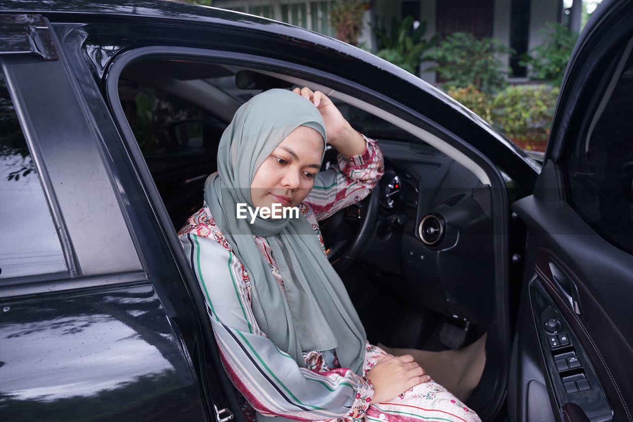 PORTRAIT OF YOUNG WOMAN SITTING ON CAR