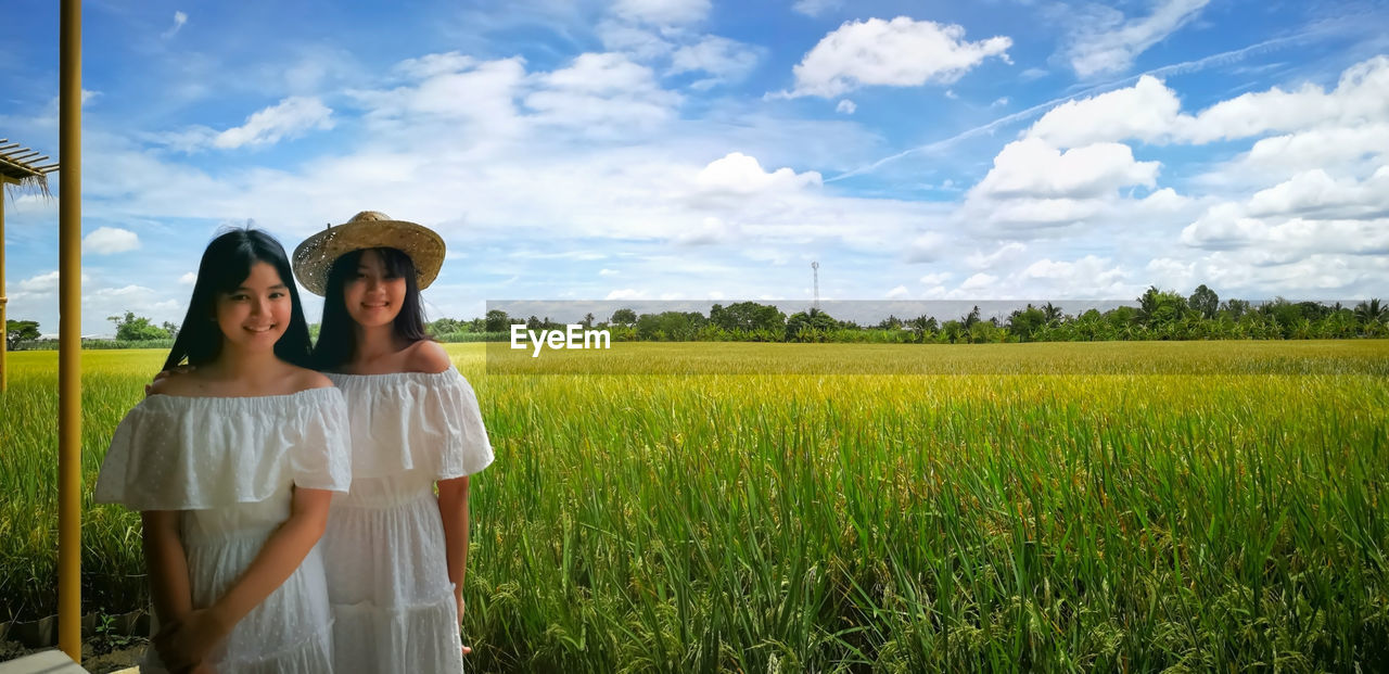 YOUNG WOMAN STANDING ON FIELD AGAINST SKY WITH TREES