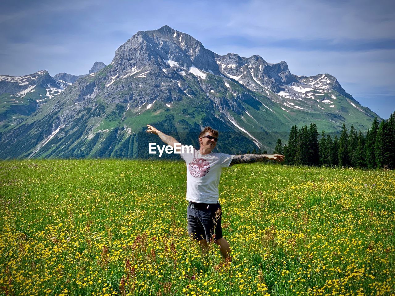 Smiling man standing on flowing land with arms raised against rocky mountain