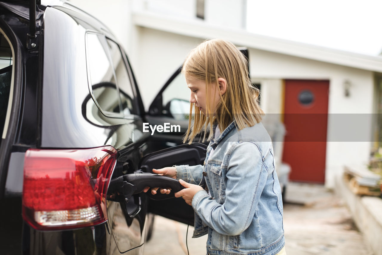 Side view of blond girl charging electric car in driveway