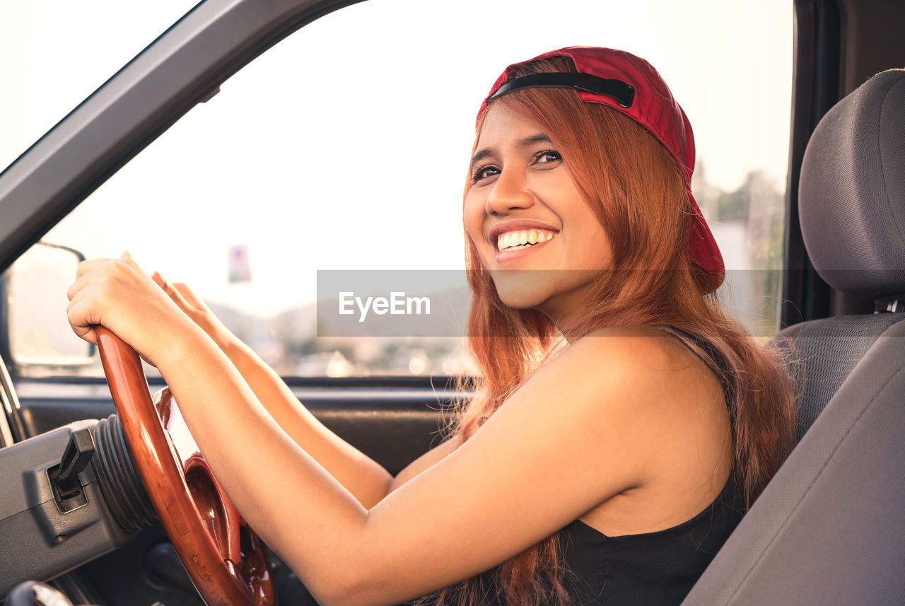 PORTRAIT OF SMILING WOMAN SITTING IN CAR