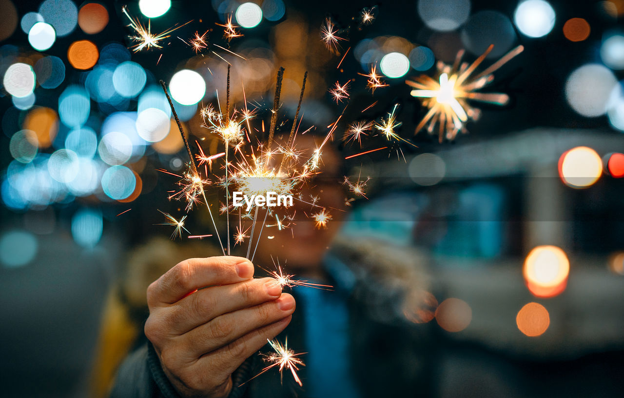 Midsection of person holding sparkler at night