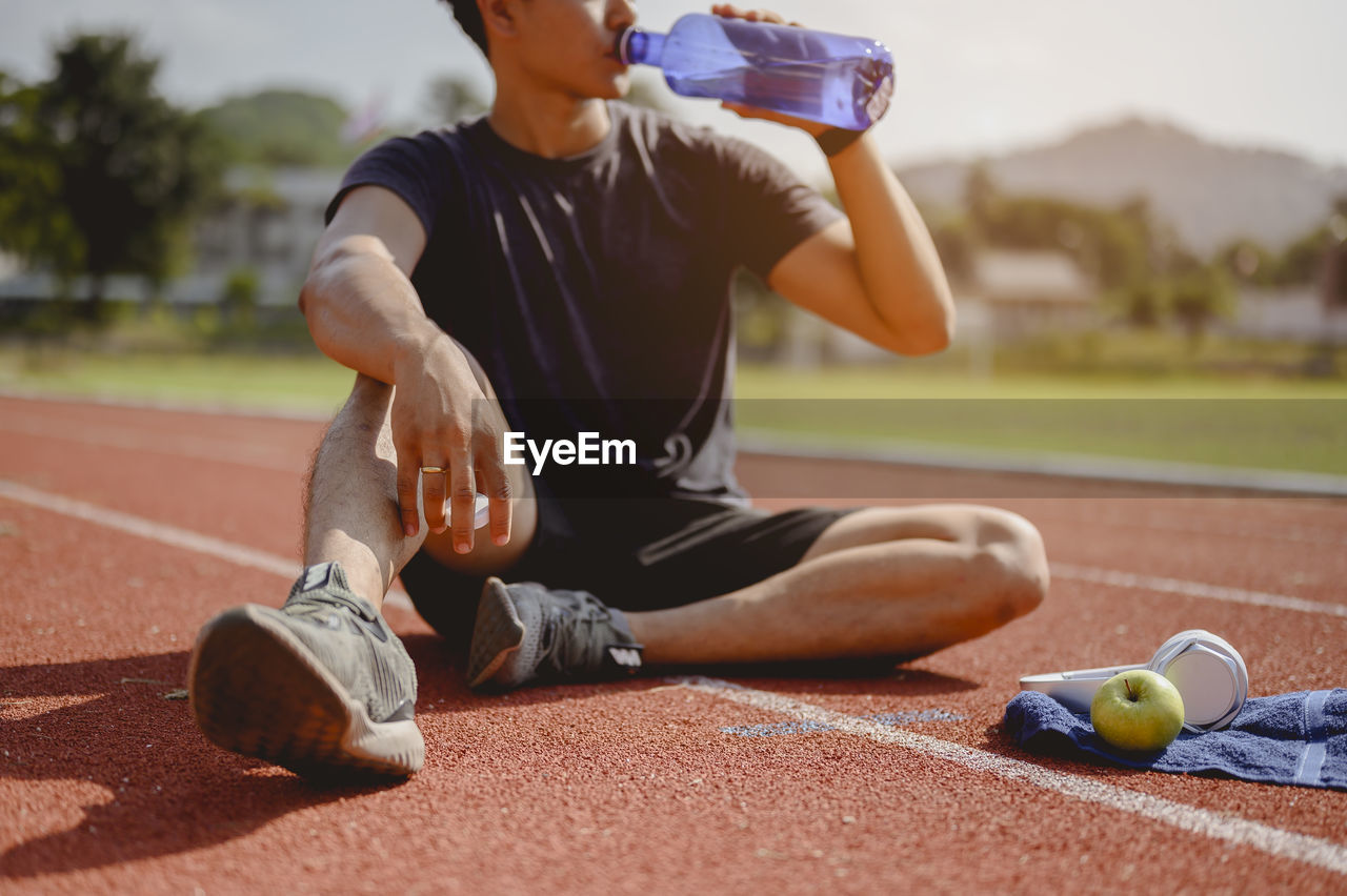 Man drinking water while sitting on running track