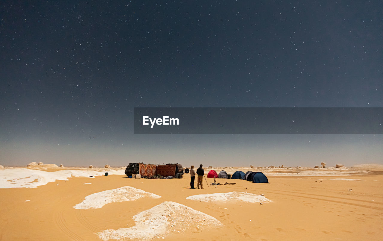 PEOPLE ON SAND DUNE AGAINST SKY