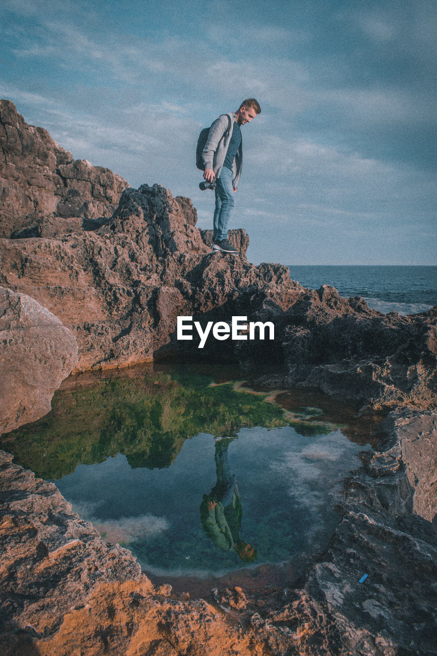 Man standing on rock by sea against sky