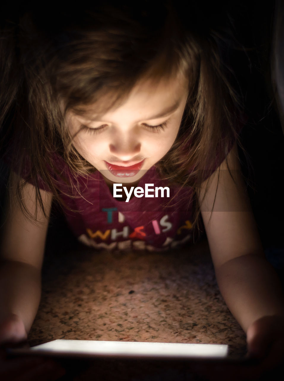 Close-up of girl using digital tablet while lying on floor in darkroom