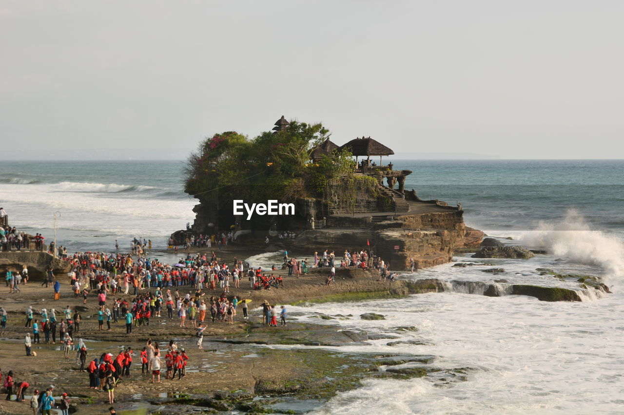 PEOPLE ON BEACH BY SEA AGAINST CLEAR SKY