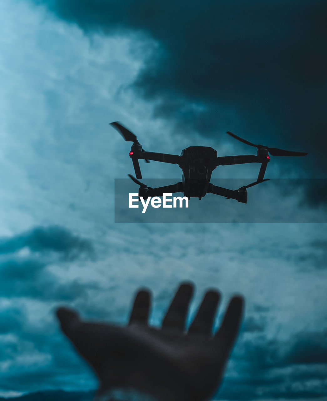 Close-up of person with drone flying against sky at dusk