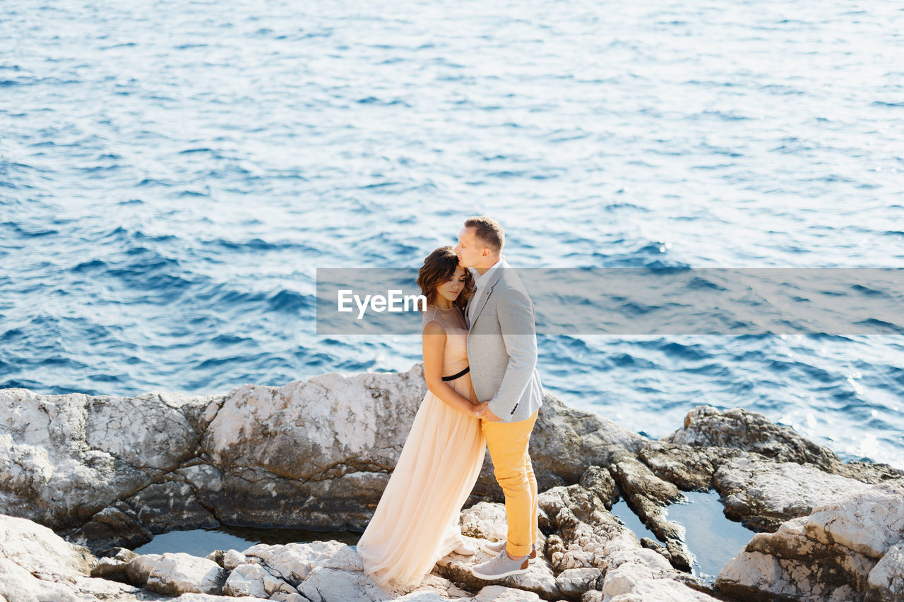 Side view of couple on rock by sea