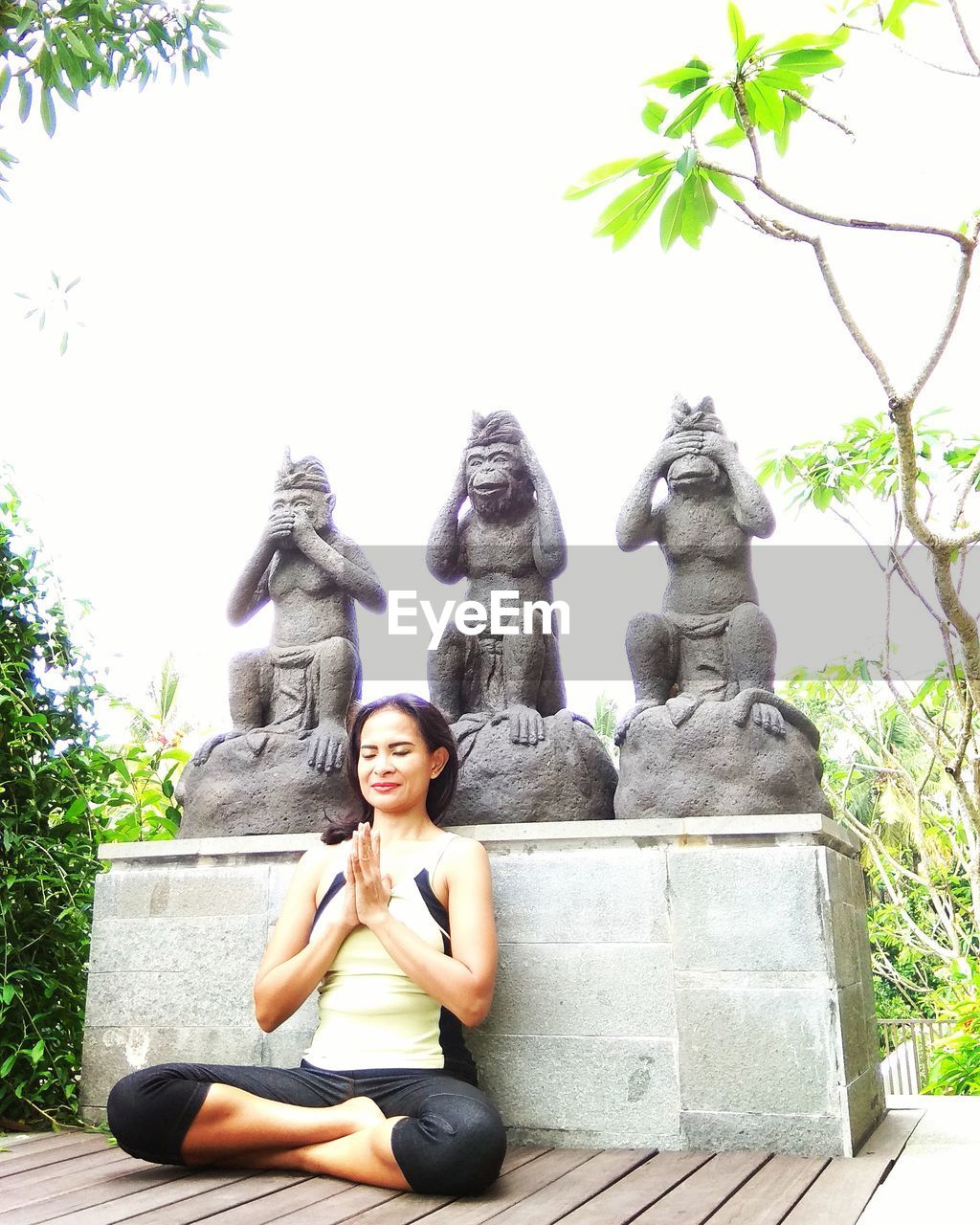 STATUE OF BUDDHA SITTING AGAINST TREE