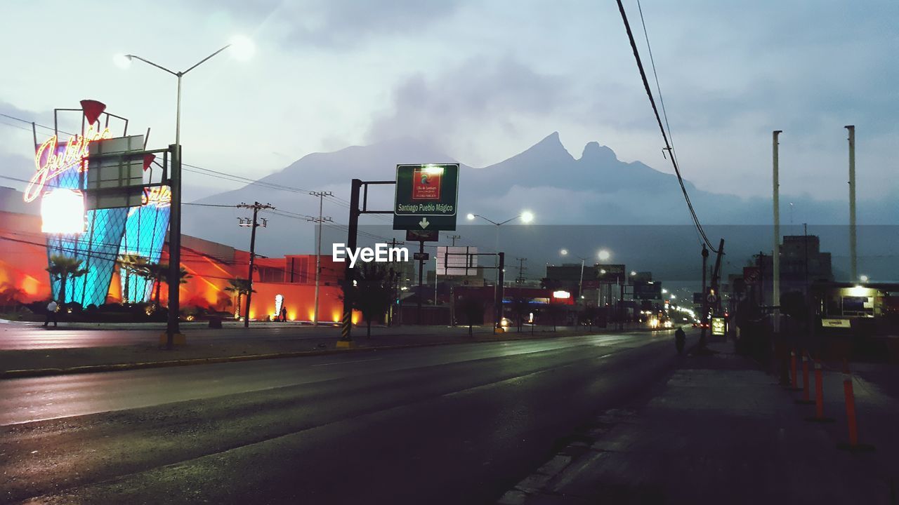 Street by illuminated buildings against mountains