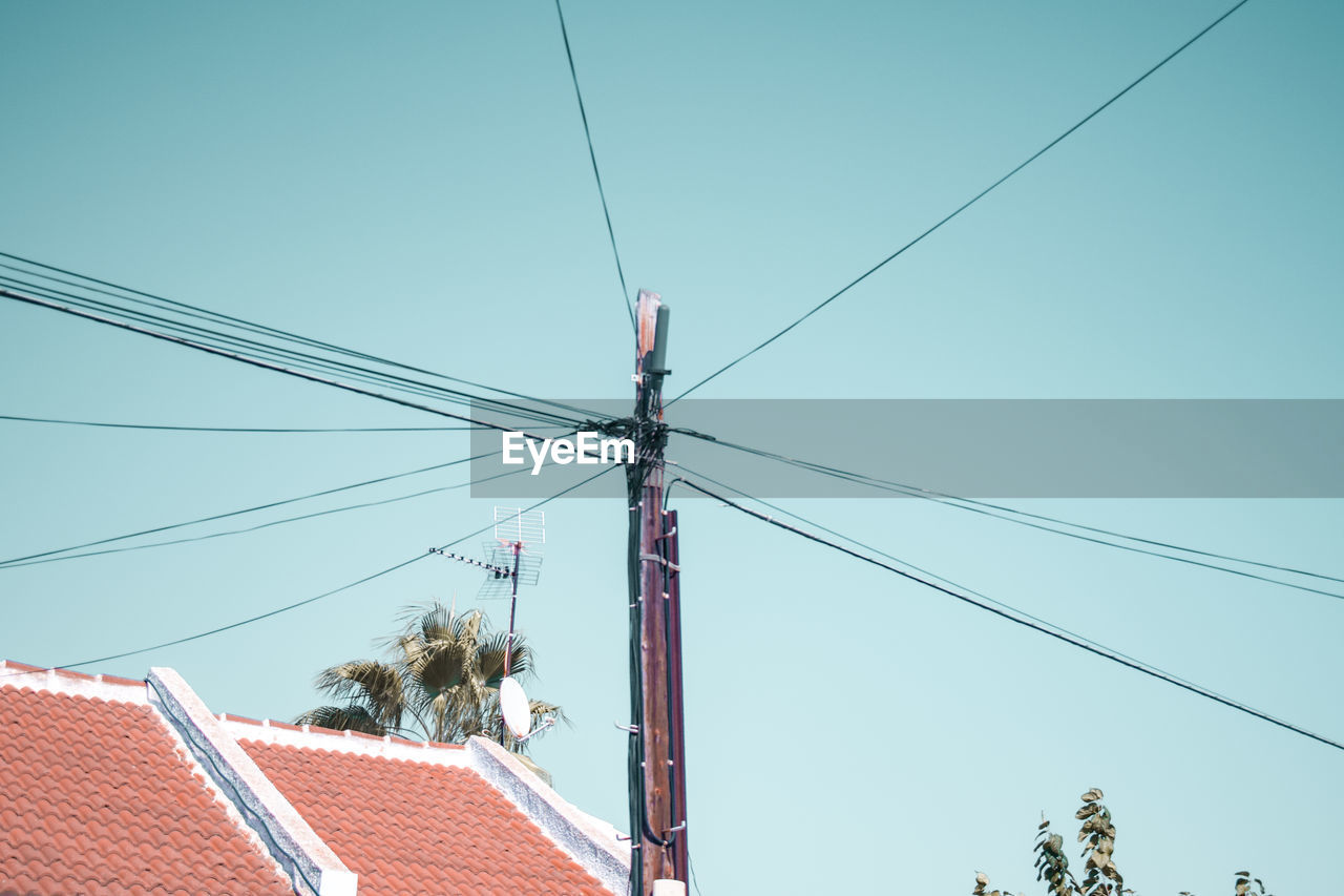 Low angle view of power lines and building against clear blue sky