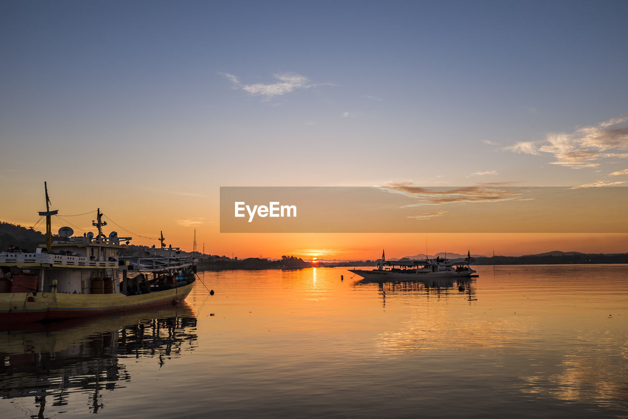 Boats moored at harbor during sunset