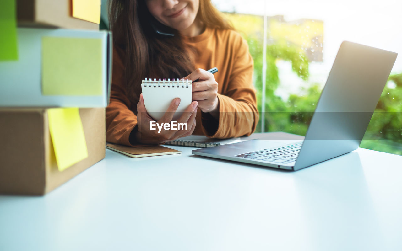 midsection of woman using laptop while sitting on table