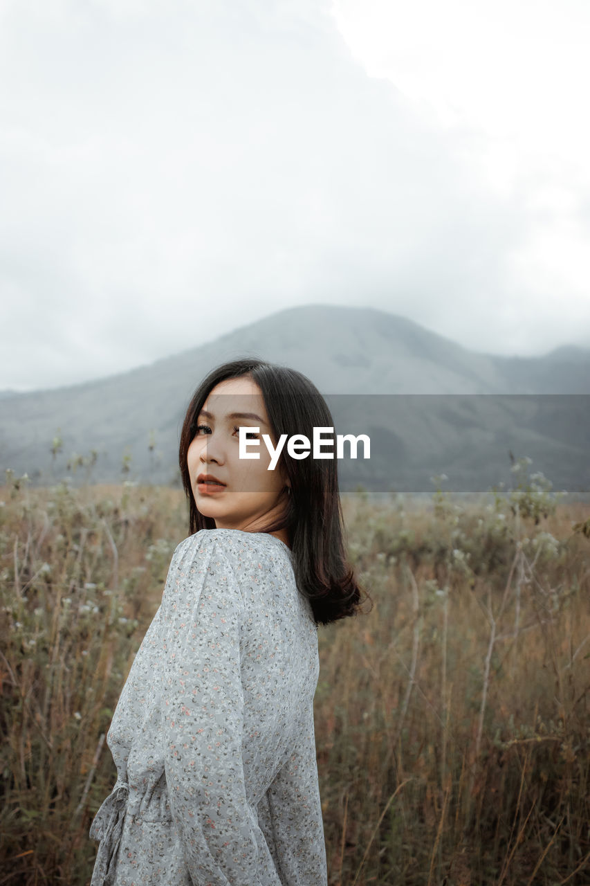 Beautiful young woman standing on land against sky